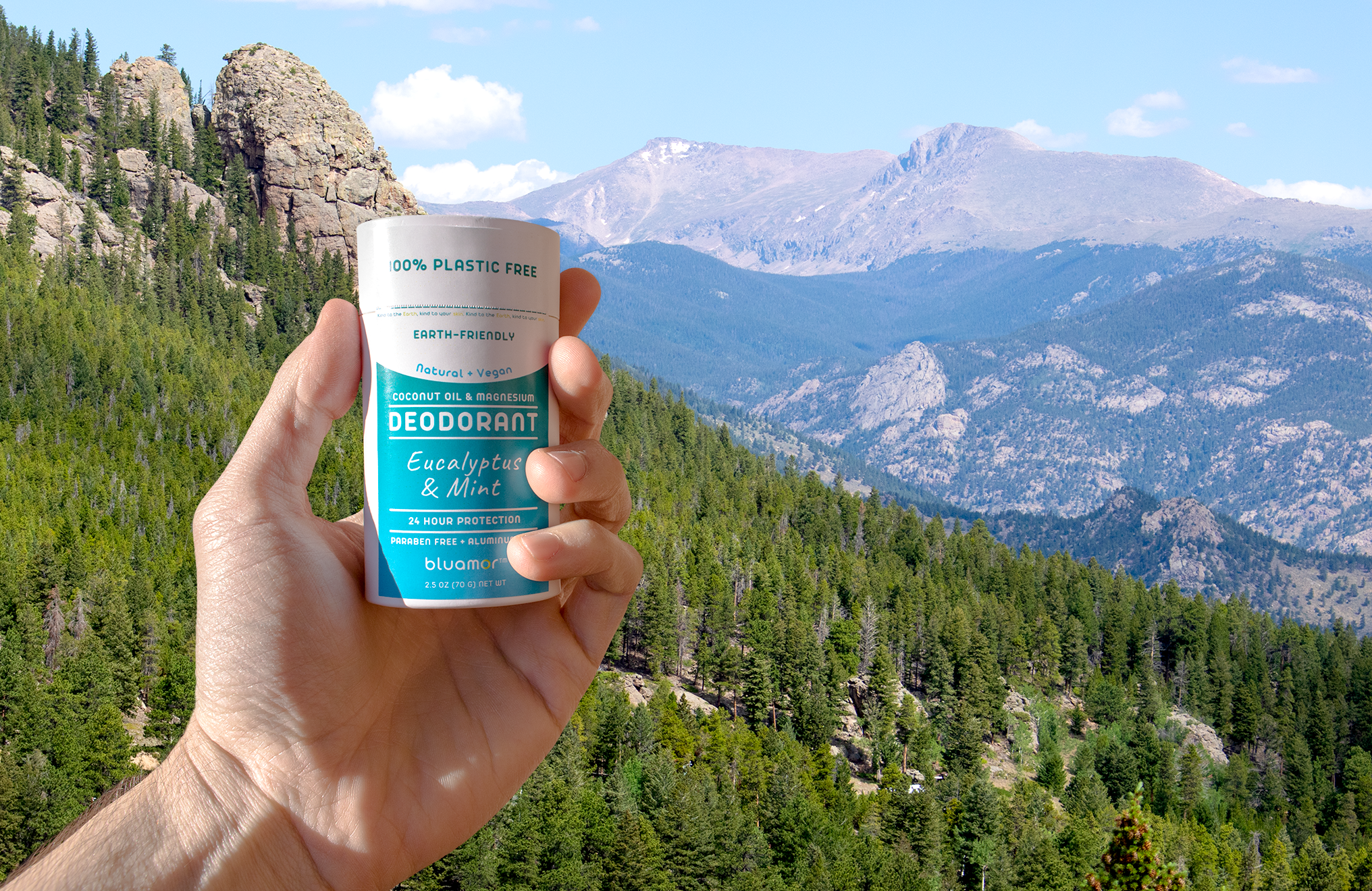 Hand holding a plastic-free deodorant container with mountains in the background