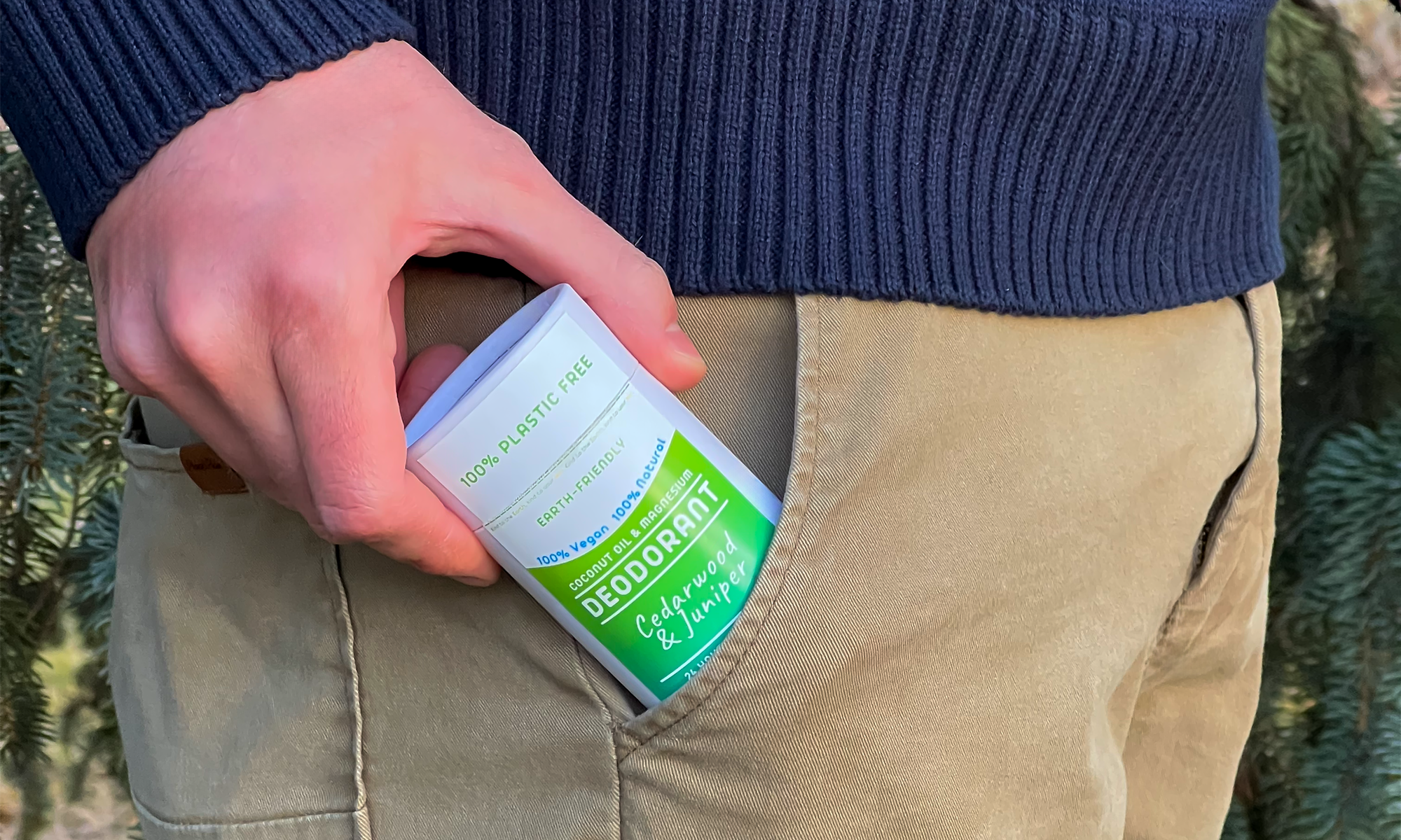 A person holds a plastic-free bluamor deodorant, labeled Cedarwood & Juniper, partially tucked in khaki pants pocket.